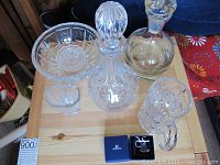 Photo showing crystal and glass items including two decanters with stoppers, cut glass bowls, beer mug, and Swarovski blue jewelry boxes with earrings and ring inside.