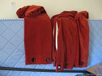 Three folded rust red velour curtain panels showing metal grommets at the edge.