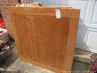 Photo of the underside of a square pine coffee table showing the top with heavy scratches and the leg attachment area with one leg broken off.