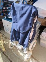 Front view of folded Emmaljunga stroller with navy fabric and chrome frame, showing wheels and canopy