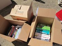 Two open cardboard boxes showing a collection of various books and audio media in sunlight.