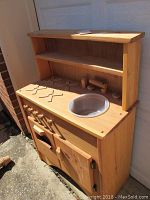 Photo of wood child's play kitchen showing countertop with sink basin and stove burner cutouts and upper shelves