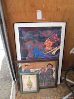 Three framed prints stacked together with the largest on the back, medium in front bottom right, and smallest bottom left front, all photographed against a wooden backdrop.