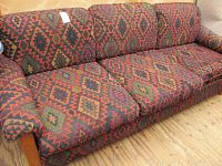 Photo of mission style wood framed sofa upholstered in red, green, black geometric patterned fabric with visible wear and wooden frame.