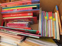 A box filled with various French children's books, organized vertically and stacked, showing colorful spines and covers, some visibly titled.