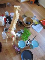Overview of lot showing giraffe figurine, glass decanter, green glasses, woven baskets, placemats, and other items on floor.