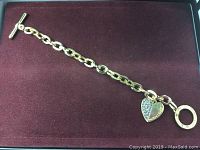 Full view of gold tone chain link bracelet on maroon background showing toggle clasp and heart charm.