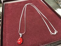 Full view of the sterling silver necklace with red jade pendant on a red fabric surface.