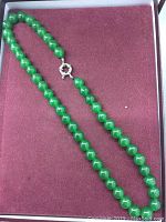 Full length view of the necklace showing the large, round green jade beads and silver tone clasp on a maroon background.