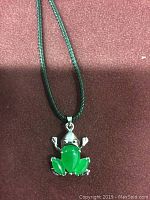 Close-up front image of green jade frog pendant on black cord necklace on a red background.