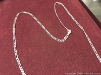 Sterling silver Figaro link necklace laid out on burgundy fabric, showing the full length and overall condition.