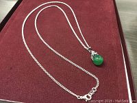Full view of sterling silver chain necklace with green jade teardrop pendant on red background