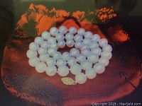 Full view of the white round pearl necklace coiled on a red fabric bag showing the 14k gold clasp.