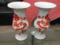 Front view of both vases side by side on glass tabletop with red fan backdrop