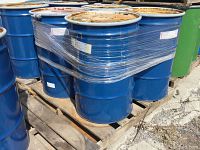 Two blue 55 gallon steel drums wrapped together on a wooden pallet. The drums show surface rust on their lids and moderate wear.
