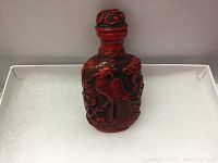 Front view showing red carved bottle with peacock design and stopper on top