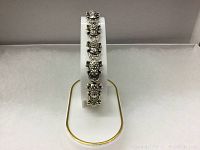 Front view of the silver tone frog bracelet on a display stand.