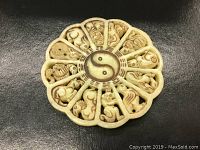 Front view of a large round scalloped pendant showing the detailed carvings of the Chinese Zodiac animals around a Yin Yang center, set against a dark black background.