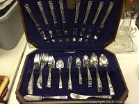 Open chest displaying the full cutlery set inside velvet-lined compartments, showing knives in the lid and forks, spoons, and butter knife on the base.