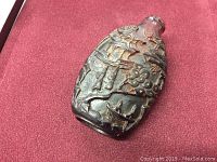 Front view of red overlay glass snuff bottle showing raised carved figural and floral landscape motifs