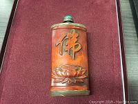 Front view showing carved floral design and script on reddish-brown ox bone surface with metal trim.