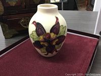 View of the front side of the vase displaying the columbine floral design in deep purple, yellow, and green on a cream background