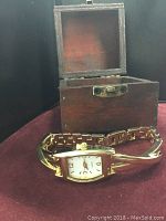 Antique wooden jewelry box open showing inside and women's gold-tone quartz wristwatch in front.