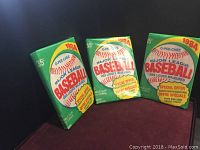 Three unopened 1984 O-Pee-Chee Major League Baseball card packs standing upright on a red surface.