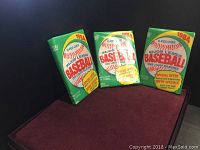 Three unopened green and red 1984 O-Pee-Chee Major League Baseball card packs, positioned upright against a dark background.
