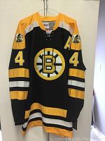 Front view of black Boston Bruins jersey showing lace-up collar, large 'B' logo, sleeve stripes, gold 'A' patch and 50th Anniversary shoulder patches