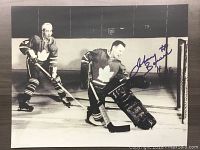 Black and white 16x20 photo print showing Johnny Bower in goalie gear for the Toronto Maple Leafs on the ice, with a teammate. Facsimile autograph on the right side.