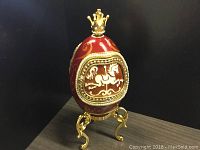 Red enamel Faberge egg with gold crown on top, decorative gold legs; detailed horse relief on front door.