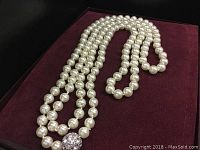 Four-strand faux pearl necklace arranged on burgundy display with round rhinestone clasp visible