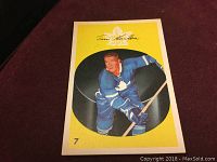 Front view of the hockey card showing Tim Horton in blue Toronto Maple Leafs uniform, holding a hockey stick with a yellow background and number 7.
