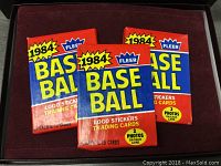 Front view of three sealed 1984 Fleer baseball card packs with bright packaging showing year and contents.