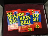 Three sealed 1984 Fleer Baseball card packs in red, blue, and yellow packaging, stacked together.