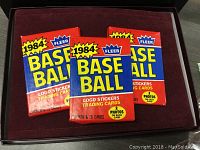 Three sealed 1984 Fleer Baseball card packs laid flat on a dark surface.