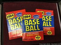Three unopened 1984 Fleer baseball card packs in blue and red packaging showing front design with year and product info.