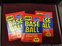 Three sealed packs of 1984 Fleer Baseball trading cards and stickers featuring logo stickers and 15 cards with 2 photos each.