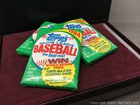 Three unopened 1984 Topps Major League Baseball card packs arranged on a flat surface with front packaging visible. Packs have green wax wrappers with colorful Topps logo and promotional text.