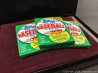 Three unopened 1984 Topps Major League Baseball card packs displayed on a dark surface, showing front packaging design.