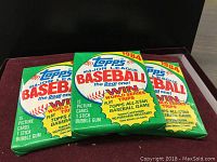Three unopened 1984 Topps Major League Baseball card packs laying flat, showing front viewing side with colorful branding and promotional text.