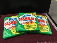 Three sealed unopened 1984 Topps Major League Baseball card packs on red cloth surface