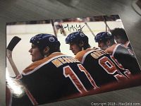 Full view of the autographed photo showing the backs of three Edmonton Oilers players: Mark Messier (#11), Wayne Gretzky (#99), and another player.