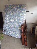 Photo showing the floral quilted mattress leaning against the wooden headboard and footboard in a garage space.