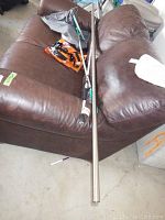 Fishing rod, Swiffer mop, steel rod, and other items on brown leather furniture and concrete floor