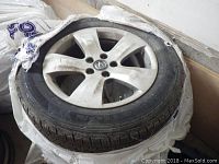 Tire mounted on silver Acura alloy rim; 5-spoke design with Acura center cap; visible dirt on tread.