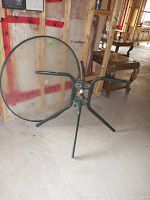 Round glass top patio table laid on its side showing glass surface and metal frame base with four legs.