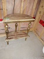 Full view of half moon table showing wood grain faux stone top, ornate gold-tone base, and lower shelf, highlighting wear on surfaces.