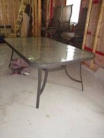 Glass top patio table showing full length, metal frame and glass surface with reflective sheen.